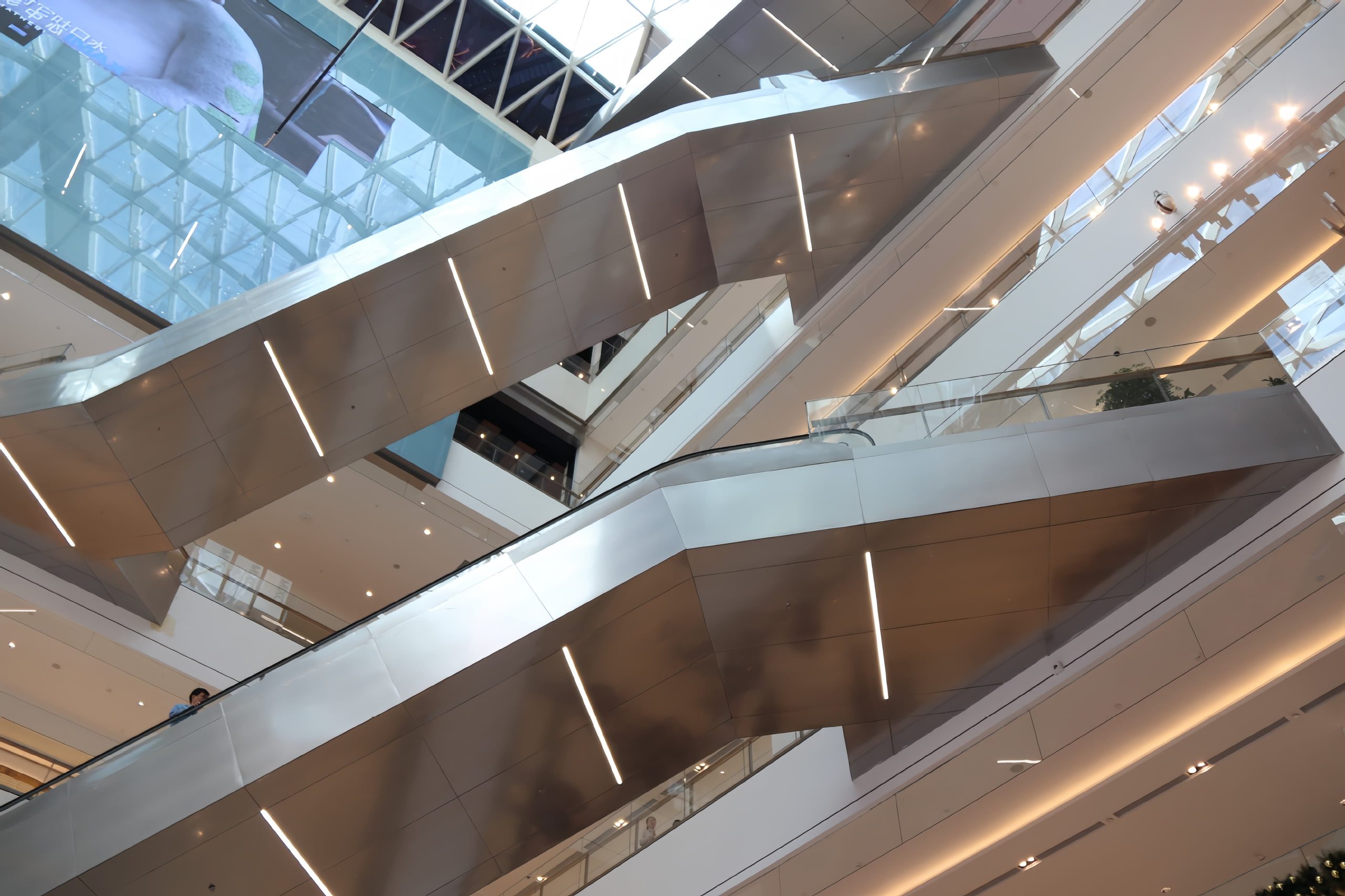 Installed stainless steel honeycomb panels serving as durable protective cladding on escalator side walls and elevator car interiors in a busy shopping mall, showcasing a smooth, reflective surface and clean joint lines.
