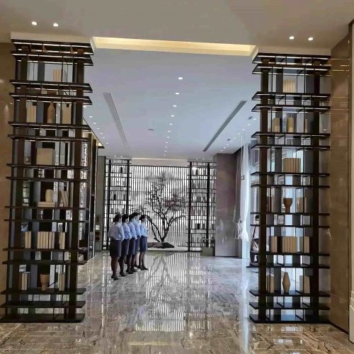Custom stainless steel decorative partition cabinet with integrated shelving, brushed metal finish, and geometric open framework, designed for high-end sales center interiors.