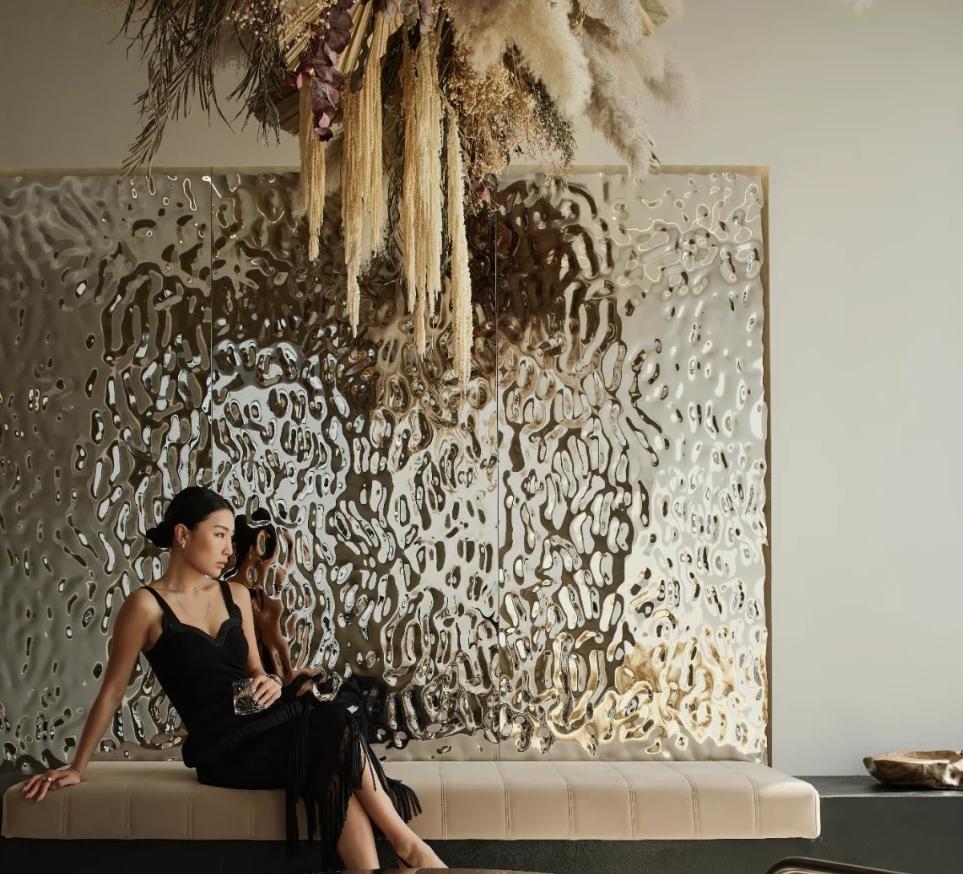 Luxury mansion interior featuring an artistic feature wall clad in water ripple stainless steel panels, flowing wave patterns, soft light reflections, and elegant metallic sheen.