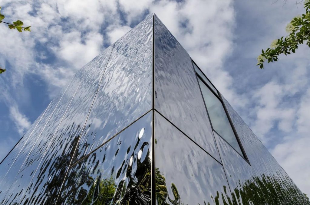 Building facade with water ripple stainless steel panels capturing dramatic shifting light and shadow, dynamic wave reflections, and striking architectural visual effects.